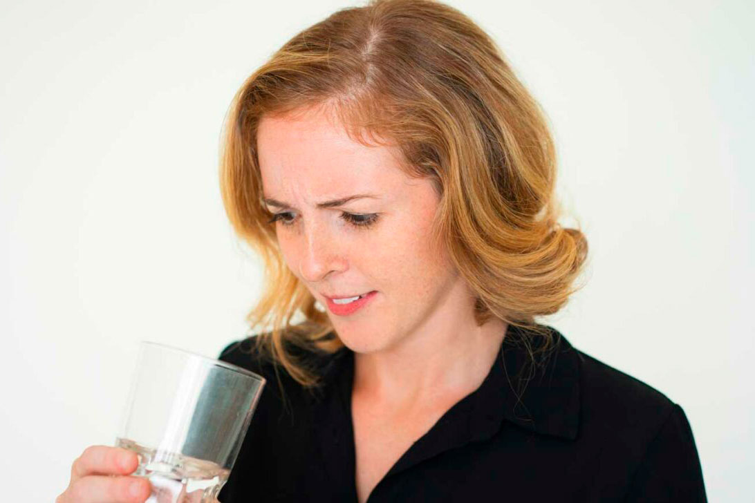 Frau in schwarzer Bluse betrachtet stirnrunzelnd und skeptisch ein Glas Wasser in ihrer Hand