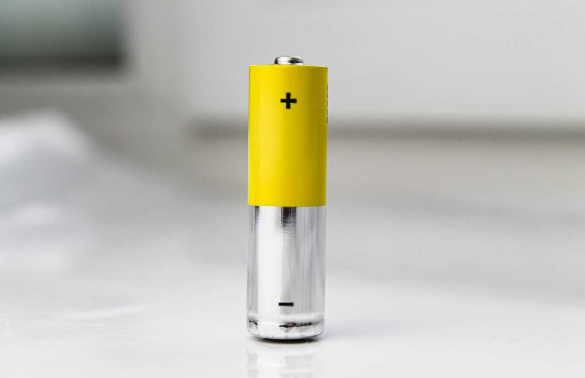 Gelbe Mignon-Batterie mit Plus- und Minuspol stehend auf heller Fläche