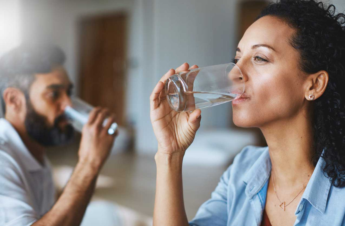 Frau und Mann trinken zu Hause nebeneinander jeweils ein Glas Wasser