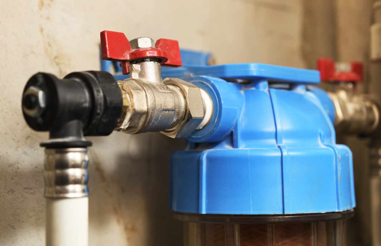 Blauer Hauswasserfilter mit rotem Absperrhahn und Verschraubung an einer Kellerwand