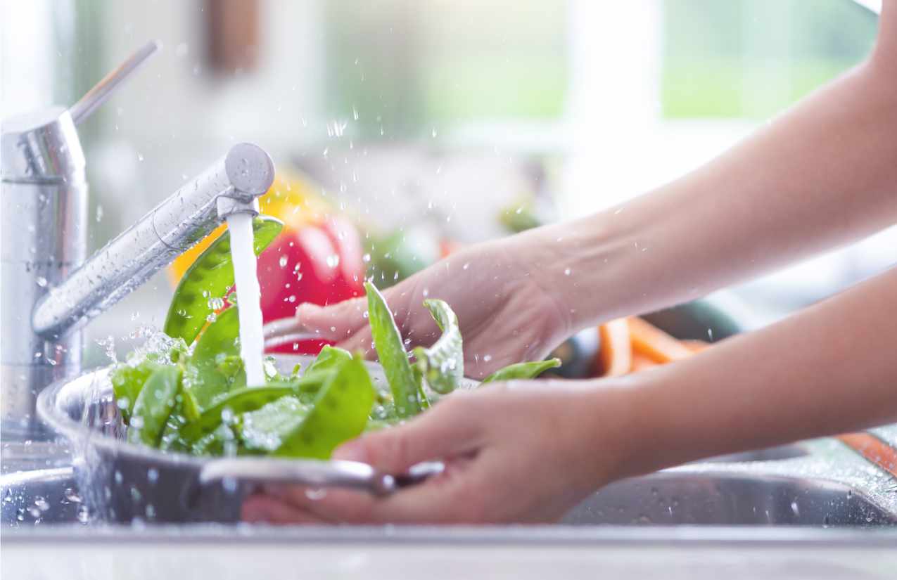 Hände waschen Paprika, Spinat und Erbsenschoten in einer Schüssel unter dem Küchenhahn