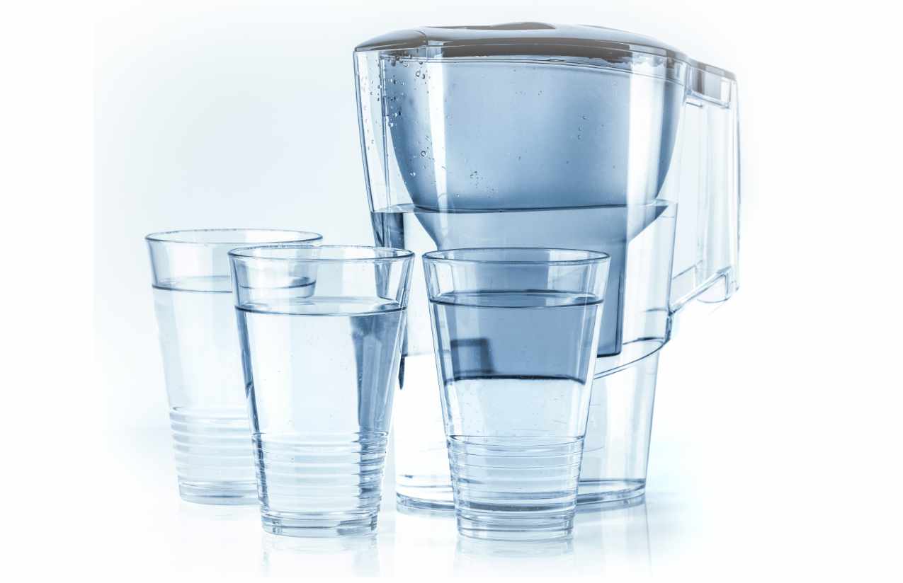 Tischkannenfilter mit Filterkartusche und drei gefüllte Wassergläser vor weißem Hintergrund